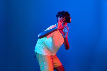 Young African American basketball gaming player wearing VR bouncing pose on blue pink neon light connecting digital futuristic technology virtual reality at metaverse world playing court. Contrivance.