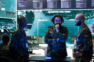 Obraz premium Team of diverse servicemen examining important real time data on a hologram projection, discussing ideas for an ongoing operation. Professional troopers work with holographic image.