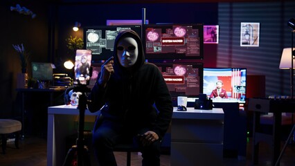 Obraz premium Hacker concealing identity filming ransom video in hidden underground base, threatening to release stolen data publicly if payout demands are not met, using phone to record blackmail footage, camera B