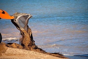 A bulldozer pushes sand to redraw the beach for erosion control.