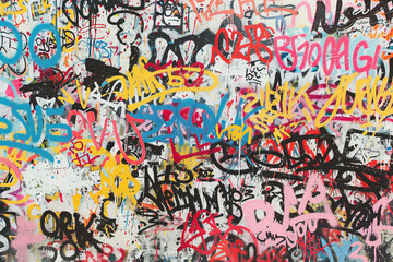 an urban wall covered in graffiti of various colors in a mix of writings and abstract designs, with overlapping letters in different sizes and styles in a chaos of colors 