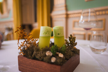 A high-end hotel interior featuring gold-accented walls, green and yellow drapery, and a unique presentation of green frothy drinks on a bed of moss.