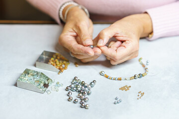 A woman collects a necklace of precious stones. View from above. Handmade. Jewelry art.