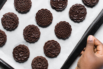 Overhead view of stamped chocolate cookies on a parchment lined baking tray, top view of embossed chocolate sugar cookies on a white background