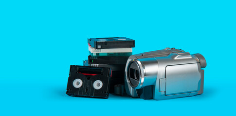 old video camera next to a black mini DV cassette tower on a blue surface against blue background