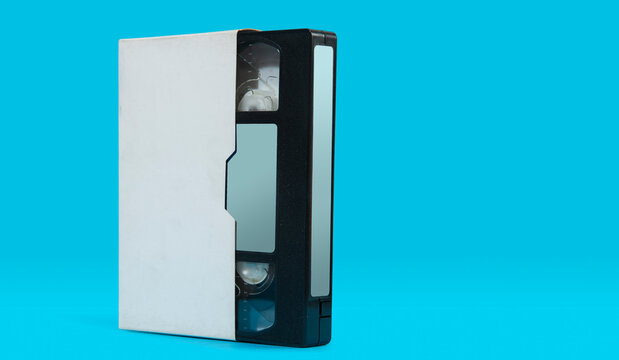 old black plastic VHS video cassette with white case on a blue surface against blue background