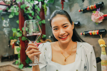 Beautiful asian female customer who likes drink wine for health : Portrait happy asian woman holding glass red wine, smelling the aroma judging the good taste and tasting good mood in a wine shop.