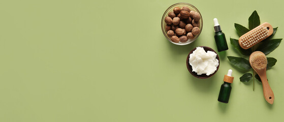 Bowl of shea butter with bottles of cosmetic oil, massage brushes and nuts on green background
