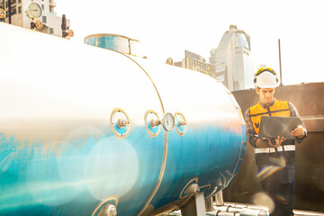 Male HAVC refrigeration system technician holds laptop recording preventive inspection refrigeration equipment Low pressure tanks contain refrigerant into the system and checked leaks ensure safety.