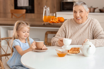 Cute little girl with her granny having breakfast at table in kitchen