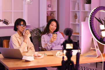 Young women with coffee cups recording podcast in studio at night