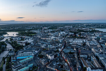 Fototapeta premium Aerial view of Galway city centre during the Pegasus Parade at twilight, showcasing the vibrant festivities and illuminated streets