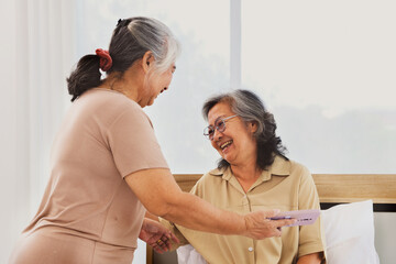 Happy elderly patient is receiving care at home from friend of the same age who uses a smartphone to video call with her family chatting giving encouragement and wishing her wel.