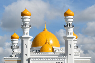 Facade of a white mosque with yellow domes and minaret tops