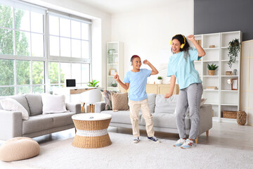 Little African-American boy with his mother in headphones dancing at home