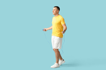 Sporty young man jumping with rope on blue background