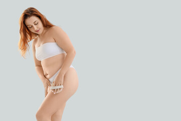 Obraz premium Young plus size woman in underwear massaging her leg with anti-cellulite brush on light background