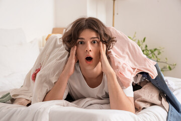 Shocked young man buried under pile of dirty laundry at home