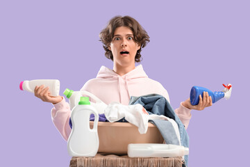 Shocked young man with dirty clothes and laundry detergents on lilac background