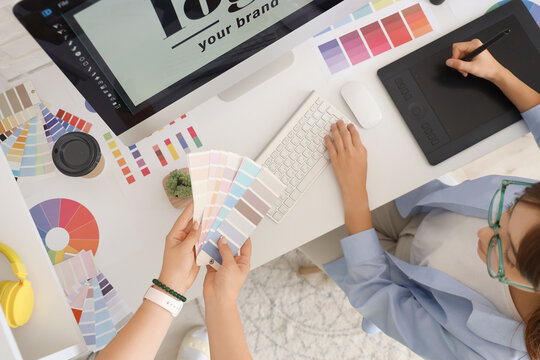 Female graphic designers working with color palettes at table in office, top view