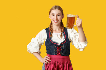 Beautiful happy Octoberfest waitress with mug of beer on yellow background