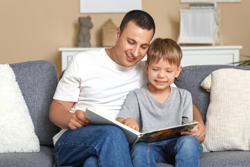 Happy father with his little son reading book on sofa at home