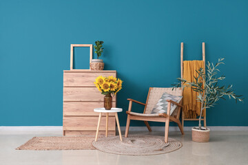 Stylish room with wooden commode and vase of beautiful sunflowers bouquet on coffee table near blue...