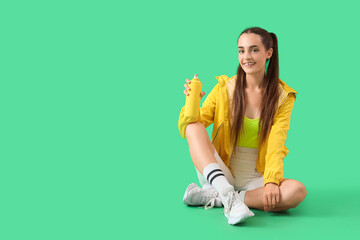 Young woman with spray paint can sitting on green background