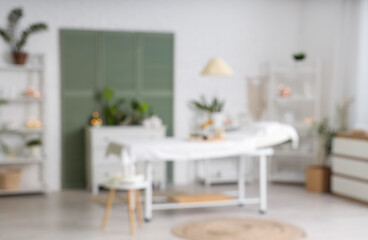 Blurred view of light spa salon with massage couch, shelf units and plants