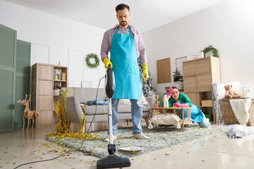 Male janitor vacuum cleaning floor in room after New Year party