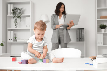 Obraz premium Cute little baby playing with cubes on desk while mother working in office