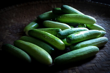 A pile of fresh cucumbers on a woven bamboo tray