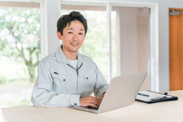 Fototapeta premium パソコン作業をする作業着・作業服姿の若いアジア人ビジネスマン 