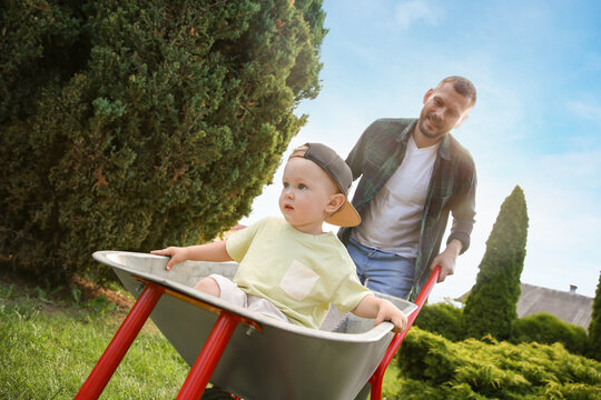 Father pushing wheelbarrow with his son outdoors, selective focus - Powered by Adobe