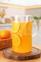 Freshly made lemonade in jug and citrus fruits on wooden table in kitchen
