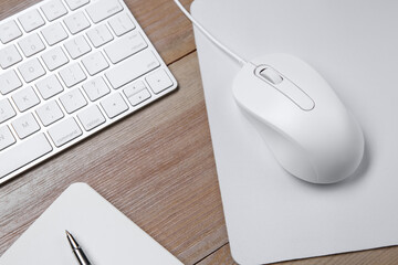 Wired mouse with mousepad, notebook, pen and computer keyboard on wooden table, above view