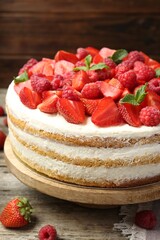 Tasty sponge cake with fresh berries and mint on wooden table, closeup