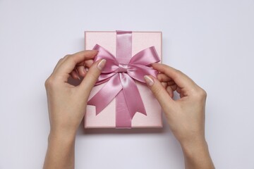 Woman decorating gift box with bow on white background, top view