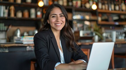 Fototapeta premium Smiling Hispanic businesswoman working on laptop in a cafe