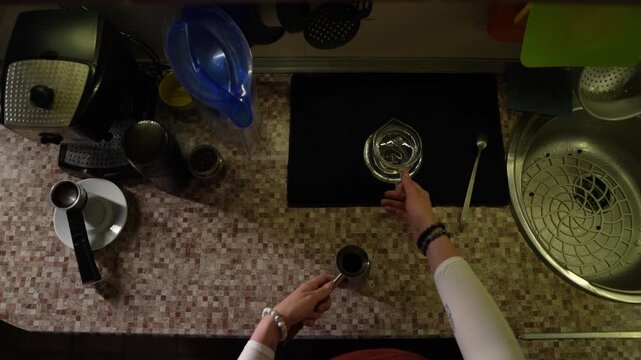 Personal perspective of woman preparing coffee in Turkish style standing in the kitchen at home. Closeup top view of female hands pouring water from glass jug in cezve. Making aroma delicious drink