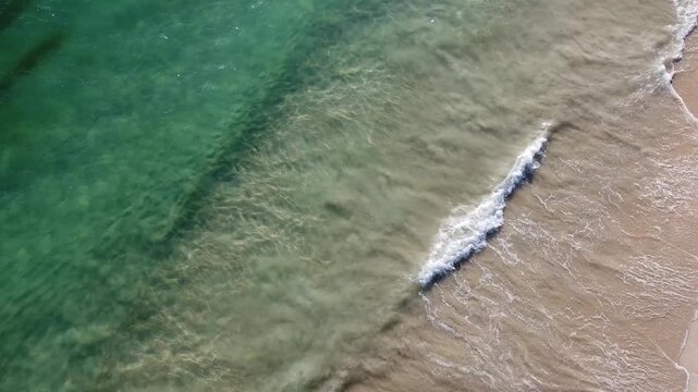 Aerial view close up of turquoise waves crashing against beach 