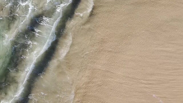Aerial view close up of turquoise waves crashing against beach 