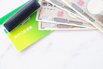 テーブルの上に置かれた銀行の預金通帳と印鑑、1万円札
