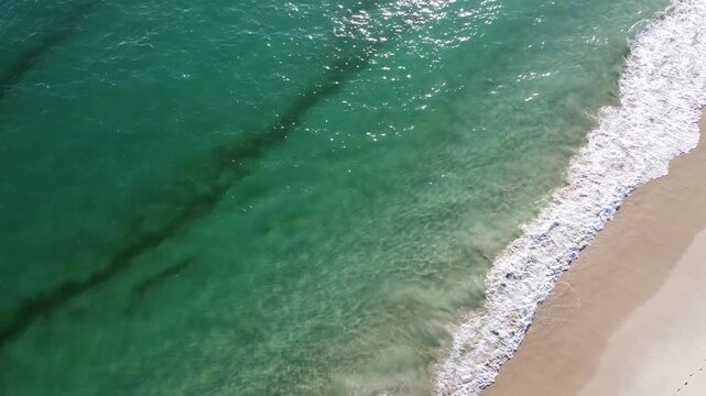 Aerial view close up of turquoise waves crashing against beach 