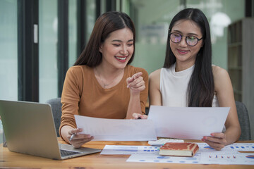 Two young Asian businesswomen discussed investment project work and planning strategy. Business people talk together on laptop computers at the office.