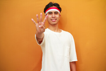 A happy Indonesian man poses counting from one to five with his fingers on a yellow background. The concept of celebrating Indonesia's independence day on August 17.
