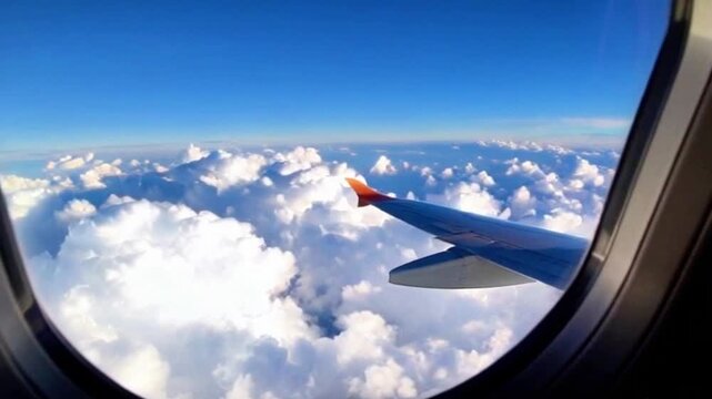 View from inside an airplane through the side window, captures fluffy white clouds drifting in a high-altitude blue sky