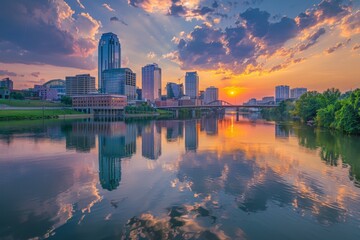 Naklejka premium Sunset over river in city, sun casting warm glow on water, buildings silhouetted against colorful sky, A serene sunset over a skyline of buildings reflecting in a calm river, AI generated