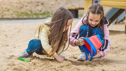 Children on the playground in the summer park. Little girls playing in the sand on the playground. Healthy active baby outdoors plays games