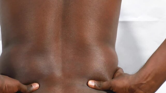 man with lower back pain severe backache, touching back trying to ease pain in spine, isolated on white background, backpain health and wellness, black man nude, medical articles .Rear view african